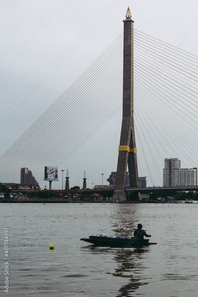 unspecify fisherman on the small boat at The Rama VIII or 8 Bridge is a cable-stayed bridge crossing the Chao Phraya River in Bangkok, Thailand. Asia.