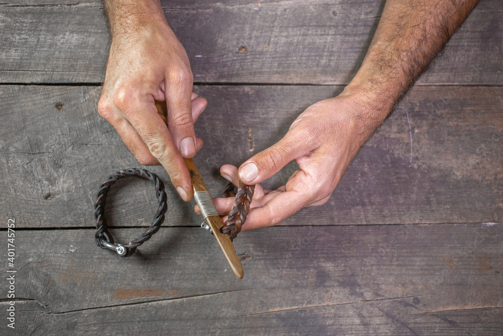 Bracelet leather handicraft. Pigtail accessory. Man s hands making handicraft leather on beautiful old wood background.