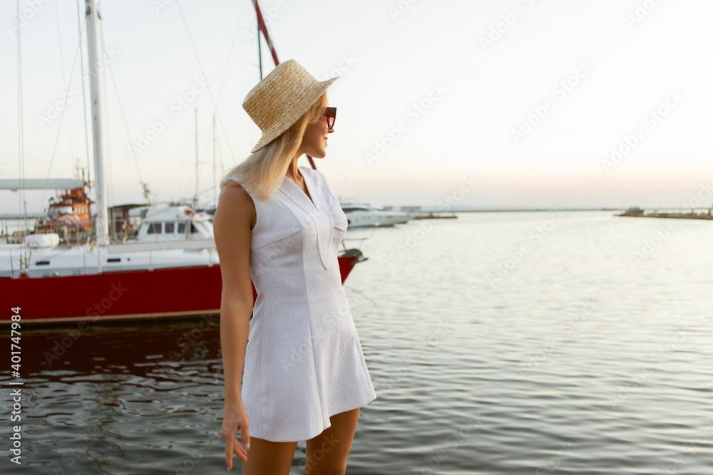 Summer portrait of young cheerful blonde woman in hat and sunglasses at sea