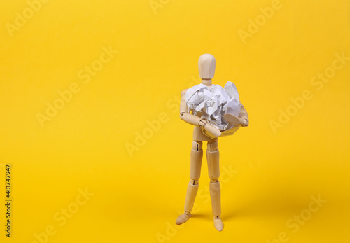Wooden puppet holding crumpled ball of paper on yellow background photo