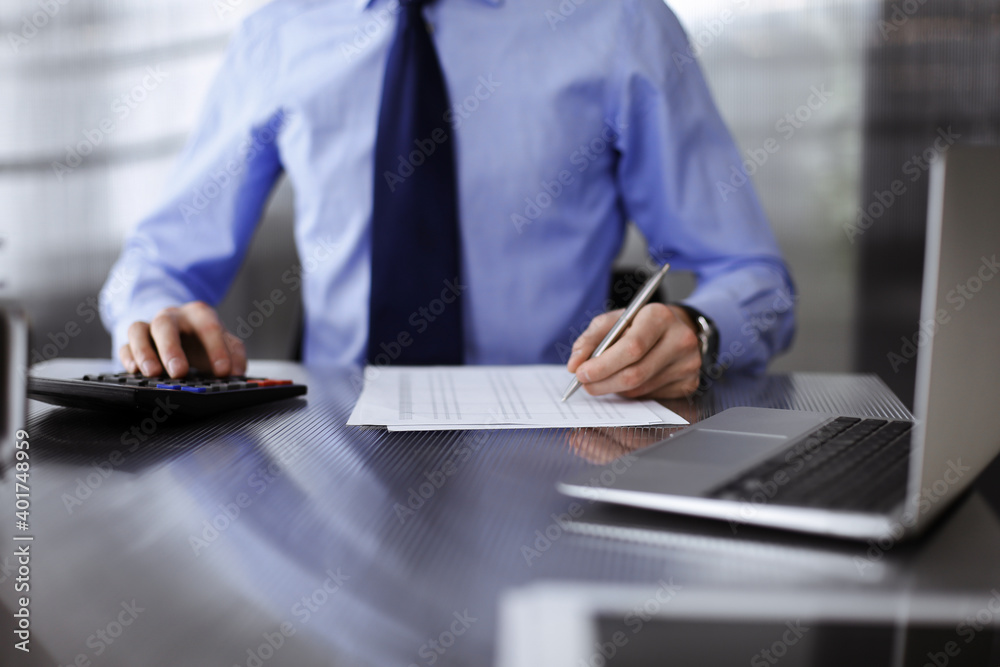Unknown man accountant in blue shirt use calculator and computer with holding pen on while staying at home during covid pandemic. Taxes and audit concept