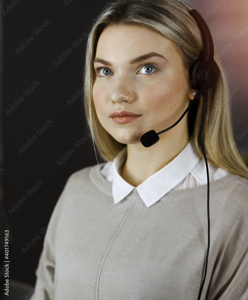 Diverse people group in sunny call center. Blonde business woman talking by headset while sitting in modern office Diverse people group in sunny call center. Blonde business woman talking by headset while sitting in modern office