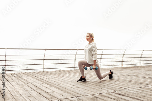 Young healthy fit woman practicing lunges with dumbbells on the city beach. Healthy lifestyle