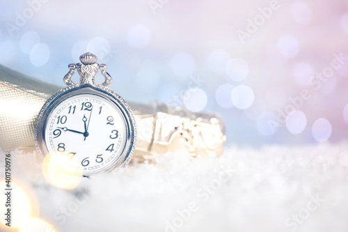 Pocket watch and bottle of champagne on snow against blurred lights, space for text. New Year countdown