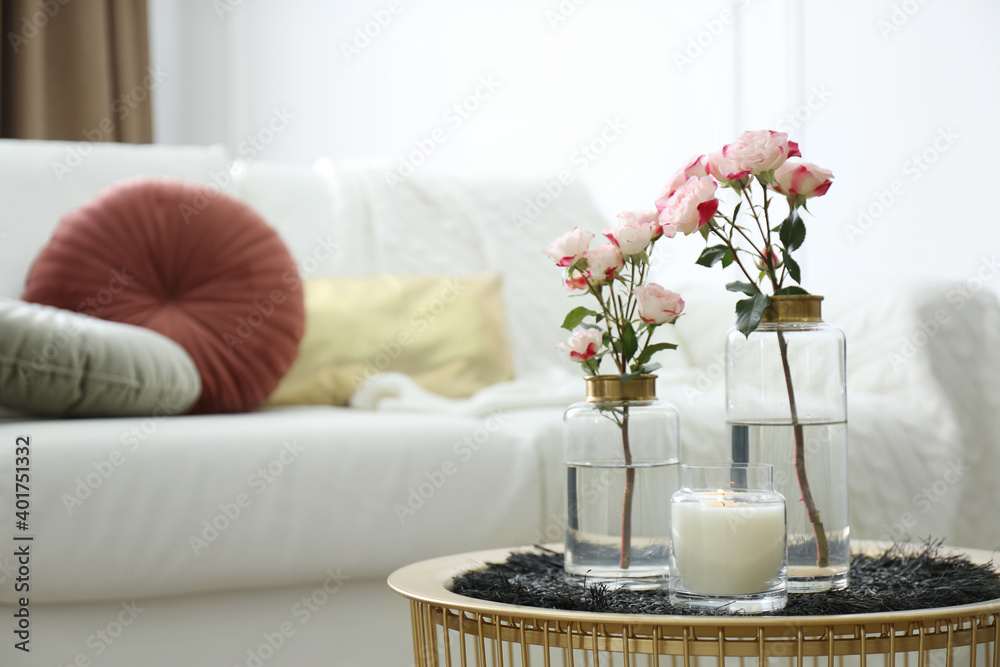 Burning candle and vases with beautiful roses on table indoors, space for text. Interior elements Burning candle and vases with beautiful roses on table indoors, space for text. Interior elements