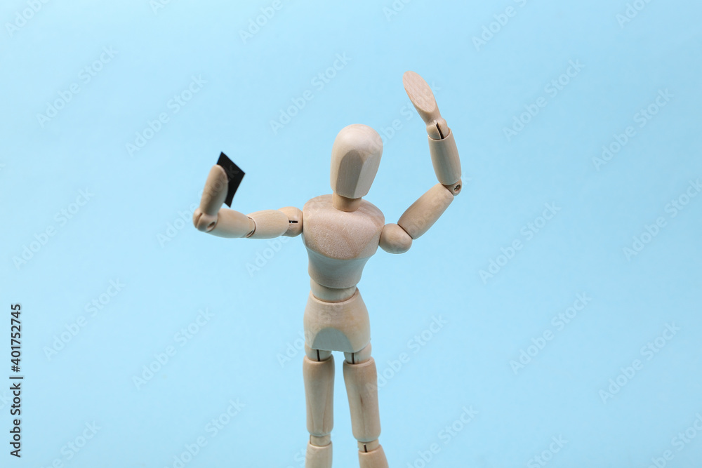 Wooden puppet makes a selfie with a smartphone in hand on blue background Wooden puppet makes a selfie with a smartphone in hand on blue background