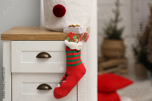 Stocking with presents hanging on drawer in children's room, space for text. Saint Nicholas Day tradition