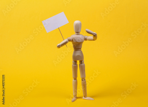 Wooden mannequin puppet standing with blank sign protesting on yellow background