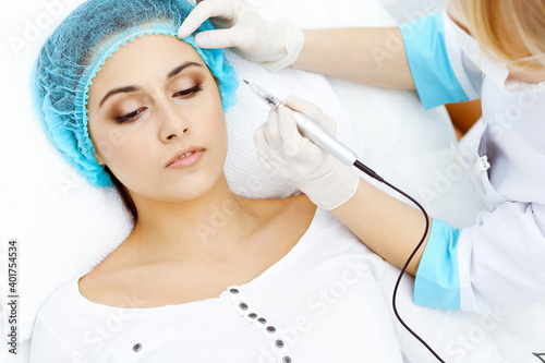 Professional beautician doing eyebrow tattoo at woman face. Permanent brow makeup in beauty salon  closeup. Cosmetology treatment