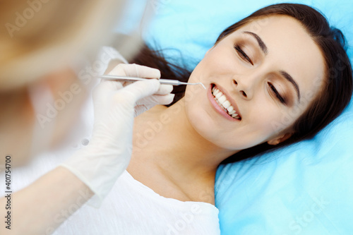 Young female patient visiting dentist office.Beautiful woman with healthy straight white teeth sitting at dental chair with open mouth during oral checkup while doctor working at teeth