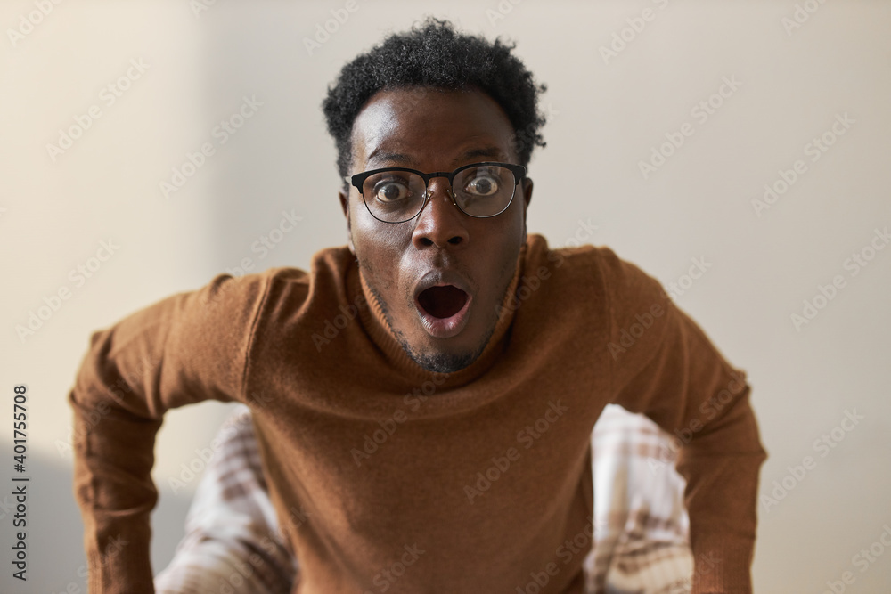Omg, No way! Funny stupefied young dark skinned man with widened eyes and mouth opened staring at camera in shock, lost for words, astonished with score, watching football game in armchair Omg, No way! Funny stupefied young dark skinned man with widened eyes and mouth opened staring at camera in shock, lost for words, astonished with score, watching football game in armchair