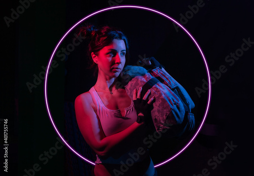Young sport woman holding a heavy fitness bag for workout in neon gradient blue red light over a dark background with circle.