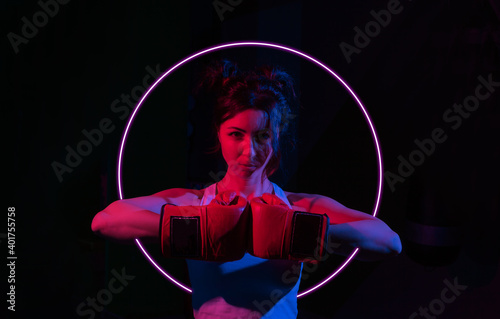 Young woman boxer with boxing gloves in a neon gradient red blue light on a dark background with glow circle.