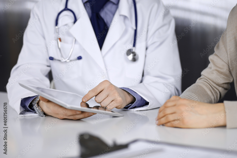 Unknown male doctor and patient woman discussing something while sitting in clinic and using tablet computer. Best medical service in hospital, medicine, pandemic stop Unknown male doctor and patient woman discussing something while sitting in clinic and using tablet computer. Best medical service in hospital, medicine, pandemic stop