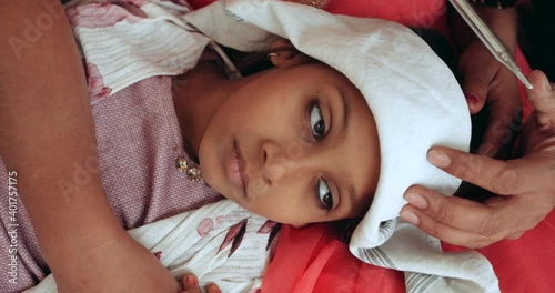 Slow-motion handheld portrait of young girl sick when parents with face masks worried care comfort help measure temperature using thermometer during lockdown new normal quarantine pandemic illness 