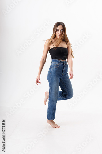young attractive asian woman with long hair in black top, blue jeans isolated on white studio background. skinny pretty female posing on cyclorama with bare feet. model tests of beautiful lady