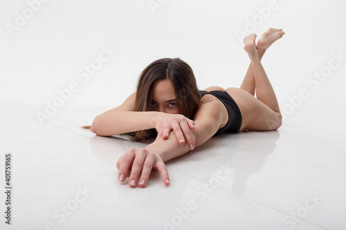 sexy asian woman with long hair posing in black lingerie on white studio background with bare feet. attractive female lying on floor on her belly. model tests of skinny lady in bodysuit