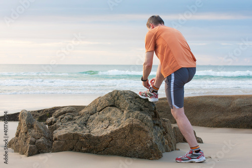 Slika na platnu Mature runner tying shoelace on a rock at a beach