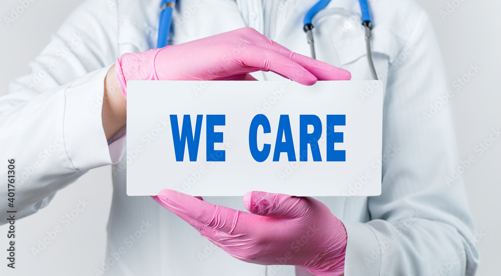 Cropped view of female doctor in a white coat and pink sterile gloves holding a card with words - we care Cropped view of female doctor in a white coat and pink sterile gloves holding a card with words - we care