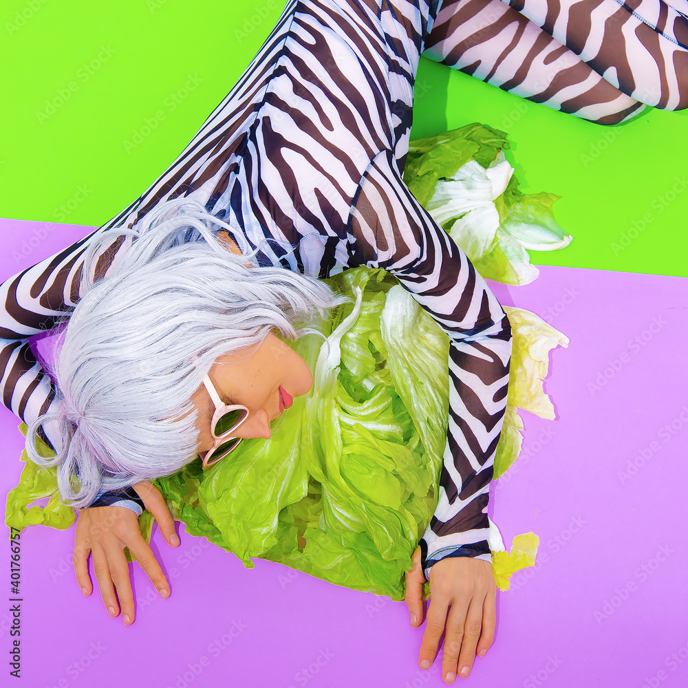 Obraz premium Blonde Girl in fashion zebra print clothes with fresh salad green background. Go vegan, animal lover. Diet, healthy food, calories concept. Raw vegan party..
