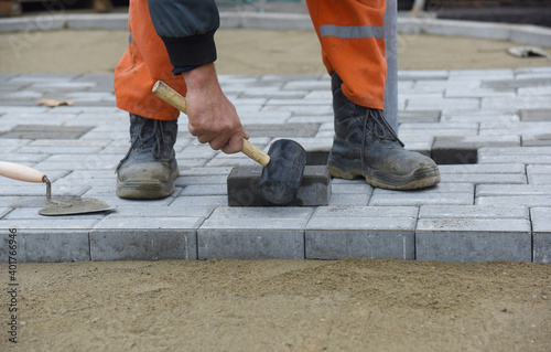 The worker lays the tile in even rows, levels it with a hammer.