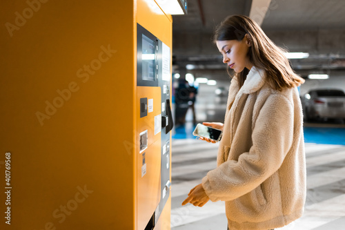 Elegant young girl pays for ticket in parking meter. Woman near terminal in the underground parking photo