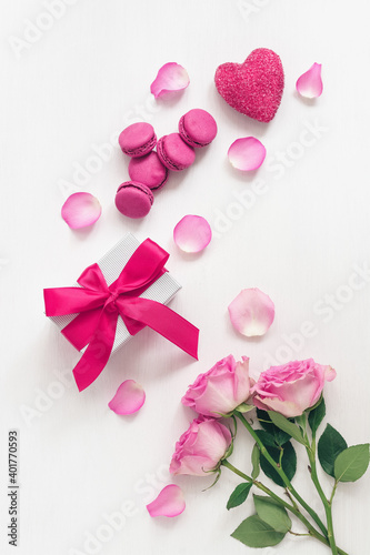 Valentine's Day. Festive breakfast. Roses, gift box, macaroon and heart decorated with rose petals. White painted old wooden background. Top view, flat lay. © Yulia