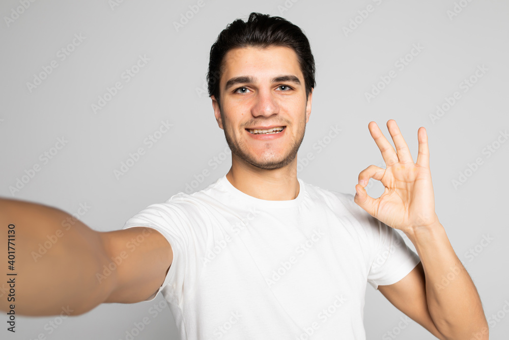 Image of excited happy young man posing isolated over white background make a selfie by camera showing okay gesture. Image of excited happy young man posing isolated over white background make a selfie by camera showing okay gesture.