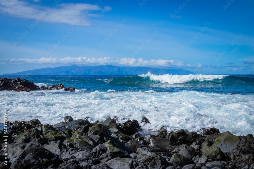 
turquoise ocean breaking waves against black beach and black rocks on a beautiful sunny day