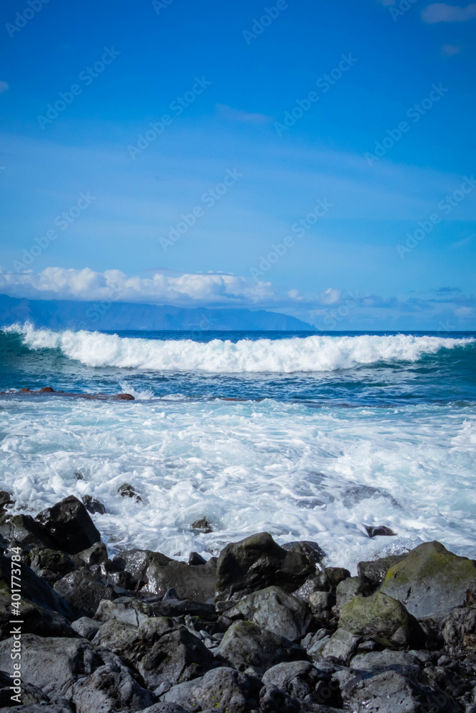 
turquoise ocean breaking waves against black beach and black rocks on a beautiful sunny day