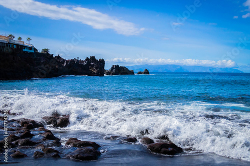  turquoise ocean breaking waves against black beach and black rocks on a beautiful sunny day