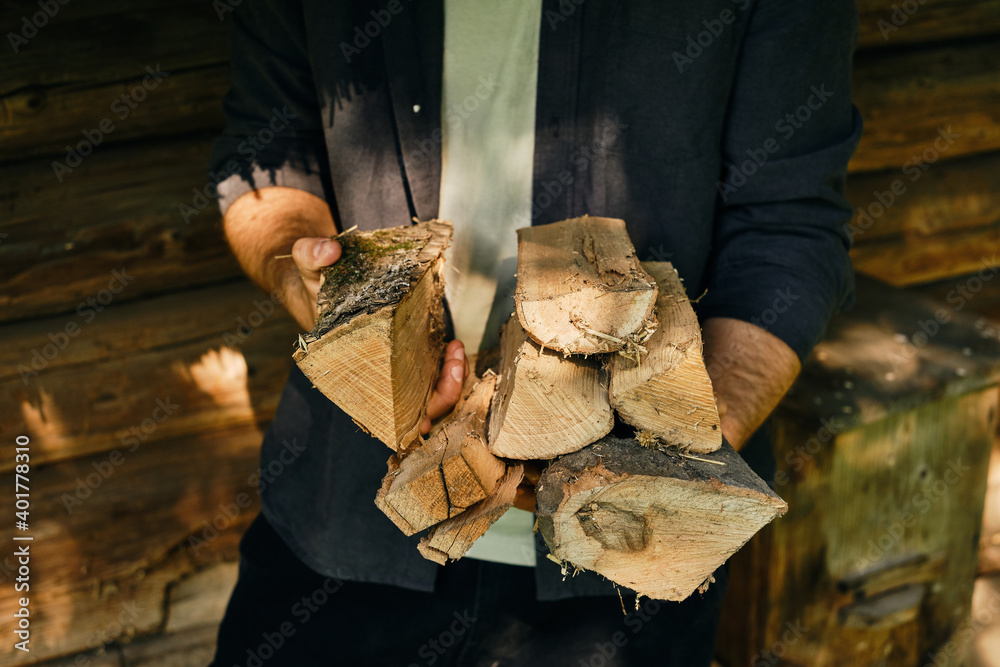 A man holds in hand firewood for a future bonfire. Preparing to light a fire in the fireplace. The lumberjack is preparing firewood for the warm in winter. Countryside lifestyle, outdoor working