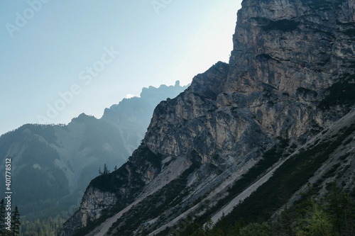 A close up view on a steep mountain wall in Italian Dolomites. There is another mountain chain behind it. The sunbeams reaching back sides of the mountain. The slopes are stony and sharp. High Alps.