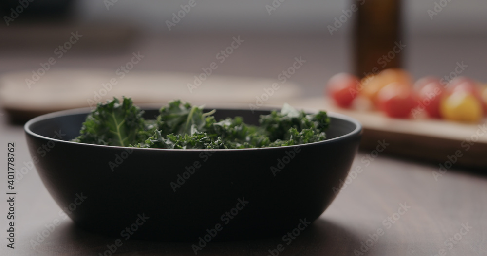 man making salad with kale, and cherry tomatoes in black bowl on concrete countertop man making salad with kale, and cherry tomatoes in black bowl on concrete countertop