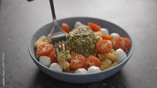 man eat pesto fusilli pasta with mozzarella and cherry tomatoes from blue bowl on concrete background