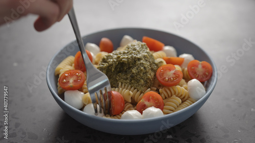 man eat pesto fusilli pasta with mozzarella and cherry tomatoes from blue bowl on concrete background