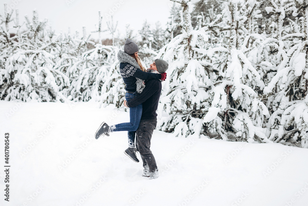 The guy holds the girl in his arms in the snowy winter forest