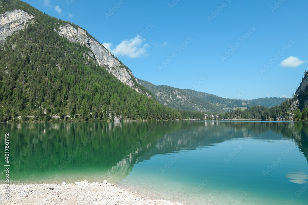 A panoramic view on the Pragser Wildsee, a lake in South Tyrolean Dolomites. High mountain chains around the lake. The sky and mountains are reflecting in the lake. Dense forest at the shore. Serenity