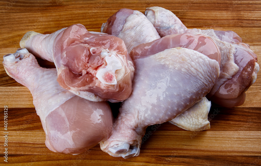 A bunch of raw chicken legs on a wooden board. Top view.