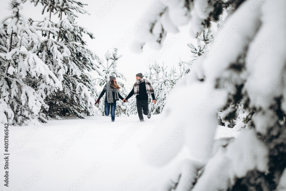 Loving couple runs through a snowy forest in winter in a sweater and a scarf and smiles