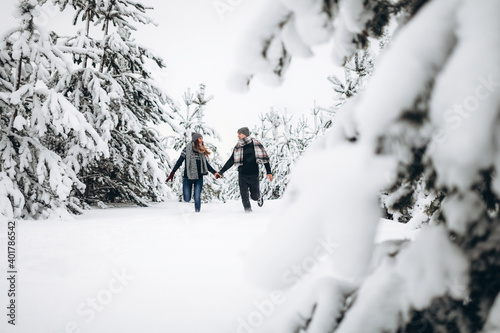Loving couple runs through a snowy forest in winter in a sweater and a scarf and smiles © Aleksandr