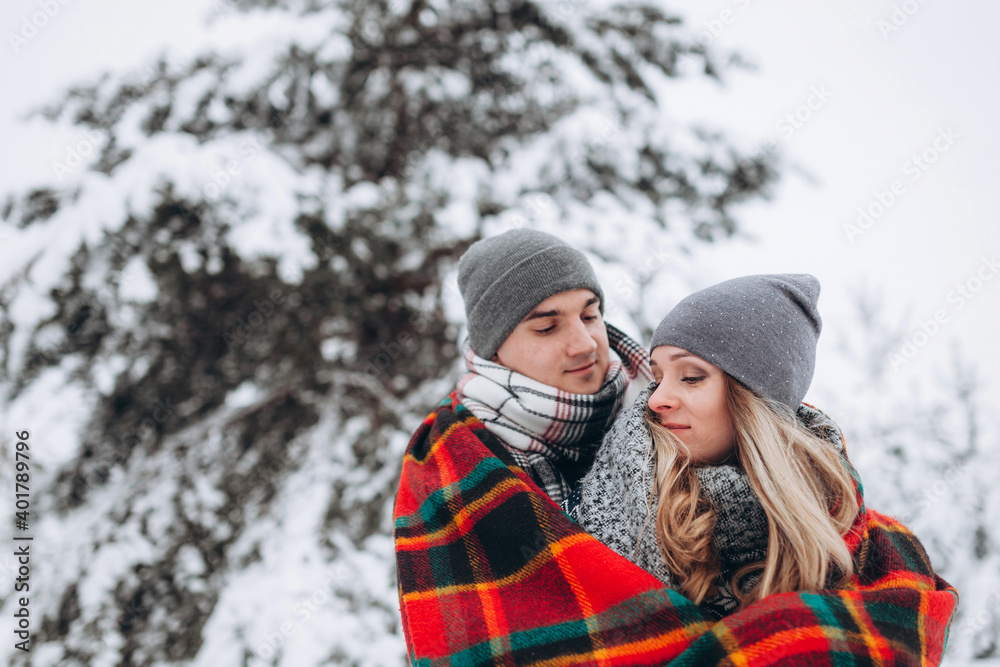 Couple in love hiding with a blanket in a snowy beautiful winter forest