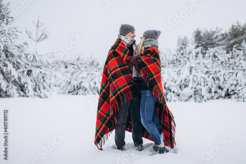 Couple in love hiding with a blanket in a snowy beautiful winter forest