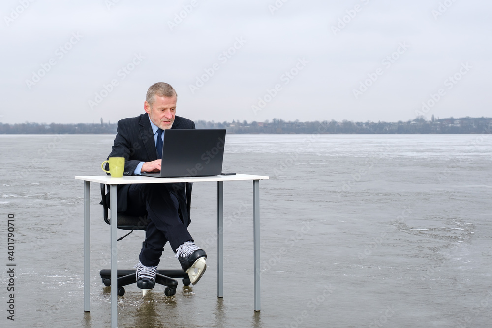elderly bearded businessman in suit and skates works with laptop on table and sitting in chair in the middle of a frozen lake. Copy space for text, work on vacation concept elderly bearded businessman in suit and skates works with laptop on table and sitting in chair in the middle of a frozen lake. Copy space for text, work on vacation concept