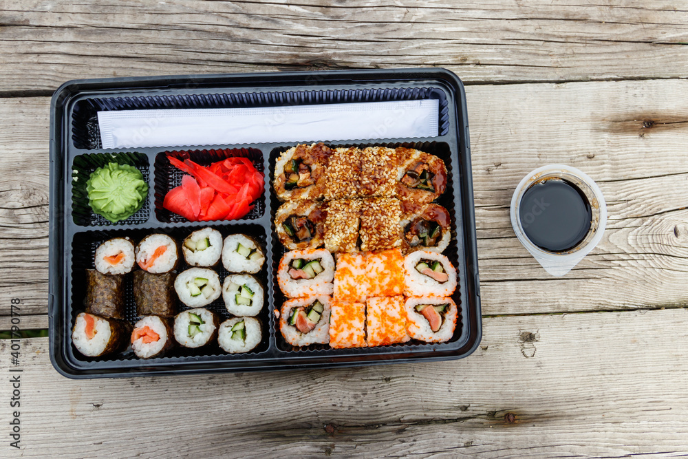 Set of sushi rolls in plastic box on wooden table. Sushi for take away or delivery of sushi in plastic container. Top view