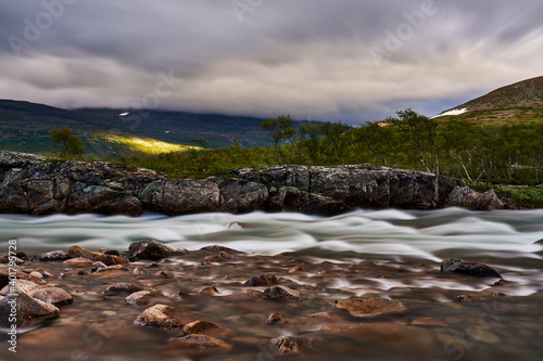 long exposure of a torrent with sun spots on the green hills in the background