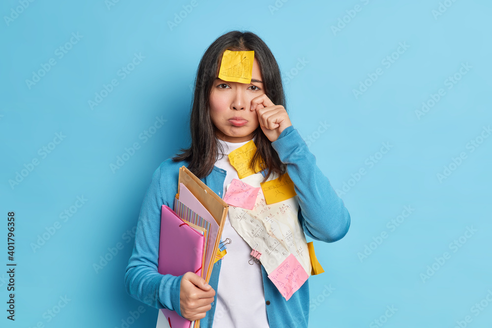Stressed tired student cries from disappointment has deadline for preparing to exam feels sad making mistake in coursework poses over blue background. Office worker has unsuccessful startup planning Stressed tired student cries from disappointment has deadline for preparing to exam feels sad making mistake in coursework poses over blue background. Office worker has unsuccessful startup planning