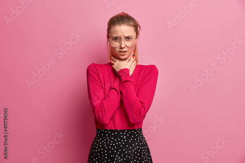 Foto Unhappy girl suffocates because of painful strangle in throat keeps hands on nec