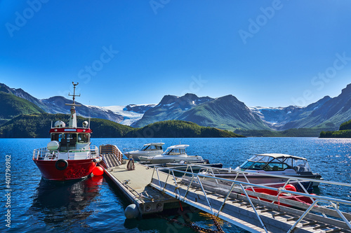 Svartisen glacier and its sourrounding moutains in the background and in the foreground a boat jetty with a big red boat photo