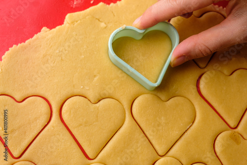  Making gingerbread cookies in heart shape using plastic cutter on the red silicon baking mat. Sweets for St. Valentines Day. 